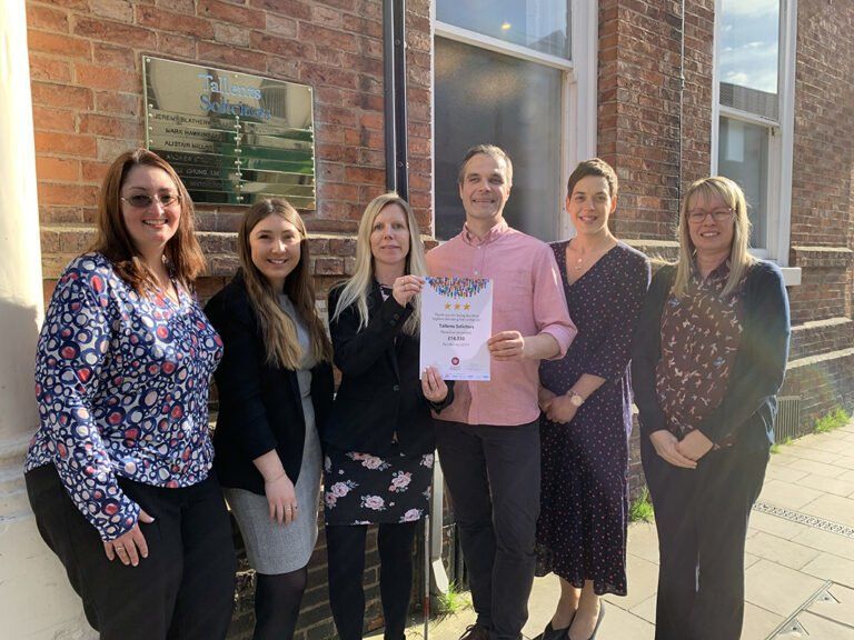 A group of people are standing in front of a brick building holding a certificate.