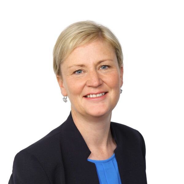 A woman wearing a blue shirt and a black jacket is smiling for the camera.