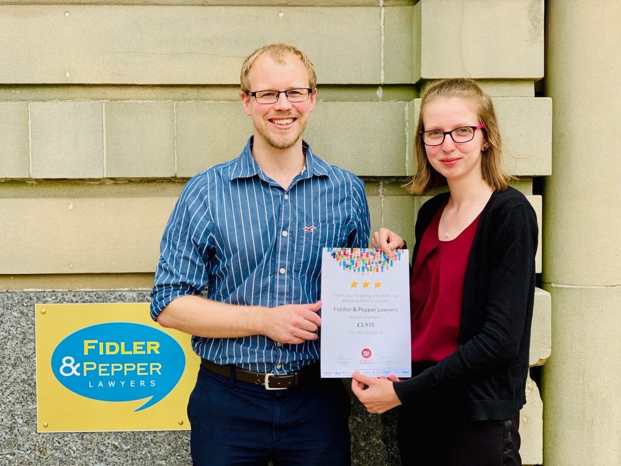 A man and a woman holding a certificate in front of a fiddler & pepper sign