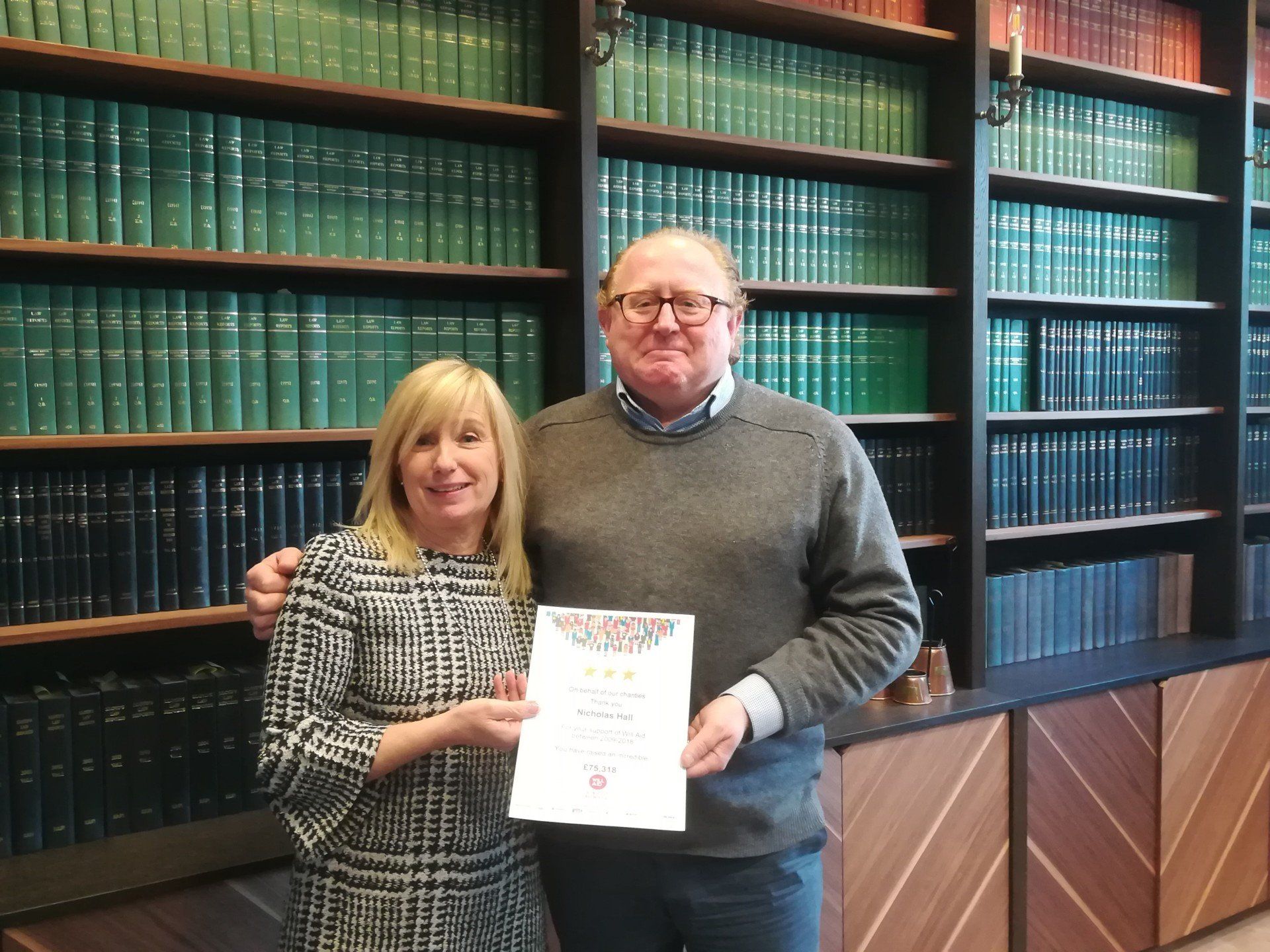 A man and a woman are standing in front of a bookshelf holding a certificate.