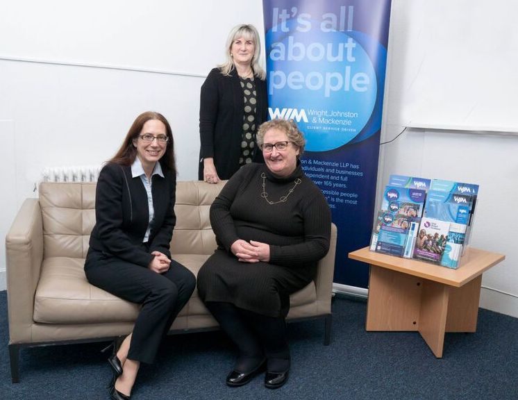 Three women sit on a couch in front of a sign that says it 's all about people