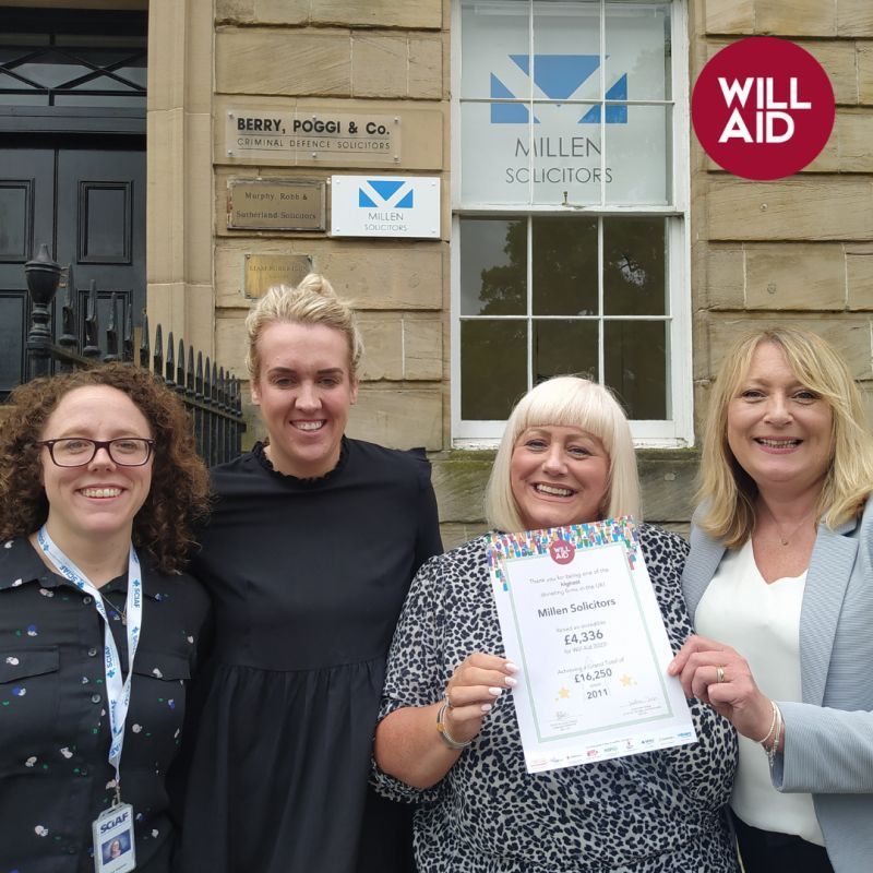 A group of women standing in front of a will aid sign