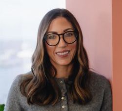 A woman wearing glasses and a gray sweater is smiling for the camera.