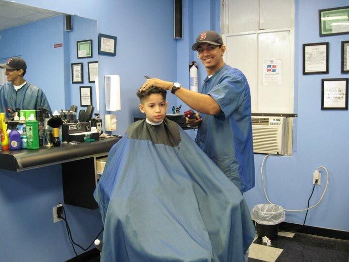 Barber cutting a child’s hair in a blue barbershop, with a cape draped over the child.