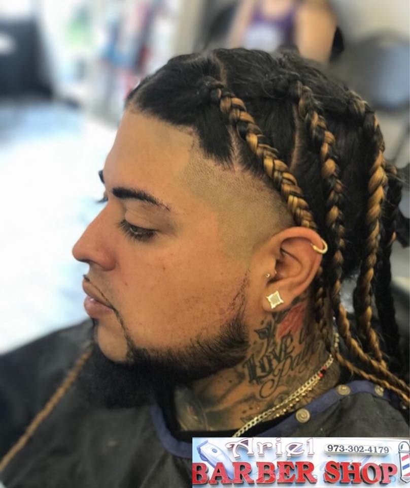 Side profile of a man with braided hair and a fade haircut, wearing earrings in a barbershop.