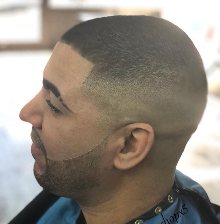 Profile of a man with a close fade haircut and lined beard in a barber chair