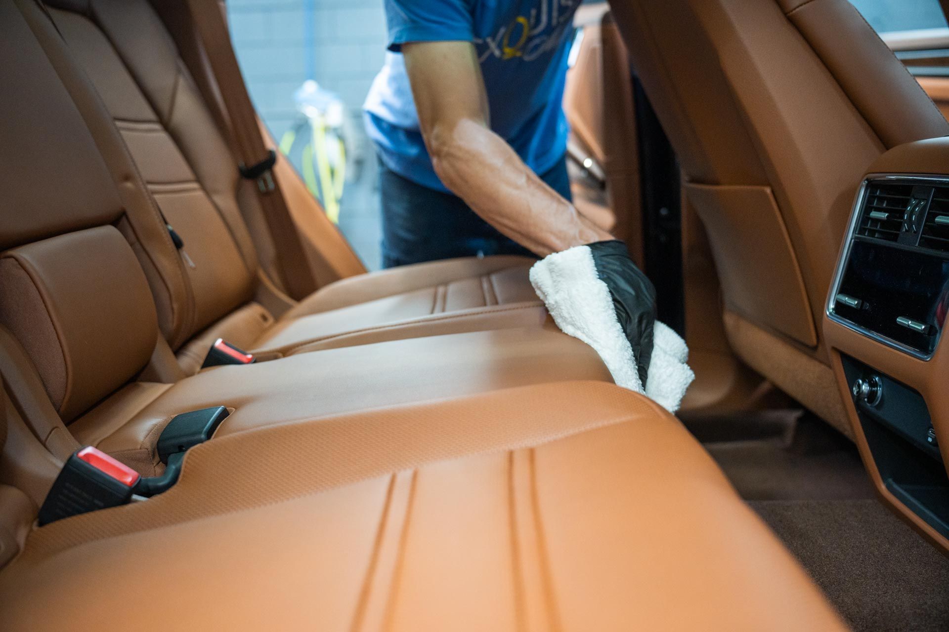 Person cleaning tan leather car seats with a white cloth.