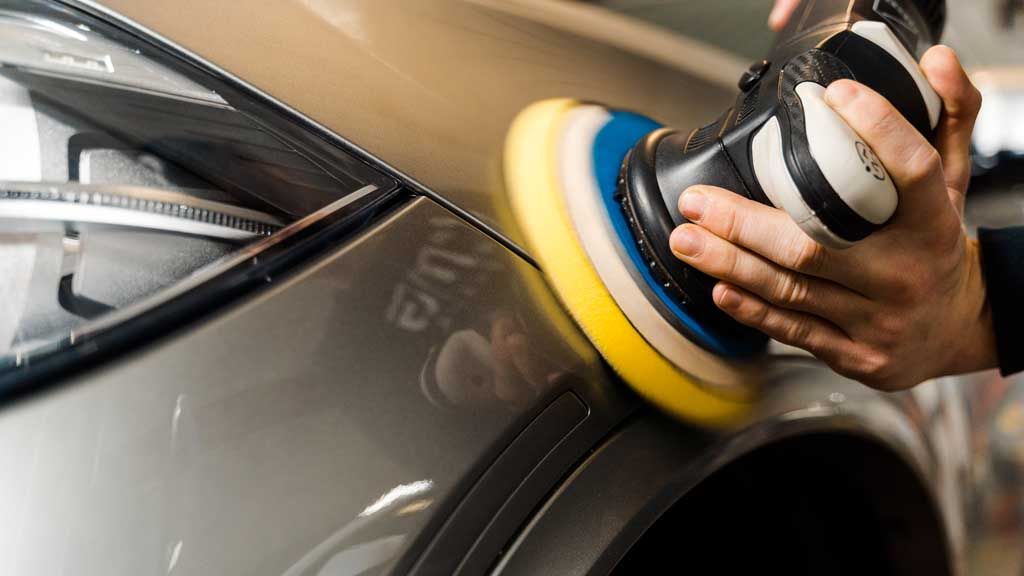 Person polishing gray car with an electric polisher; close-up.