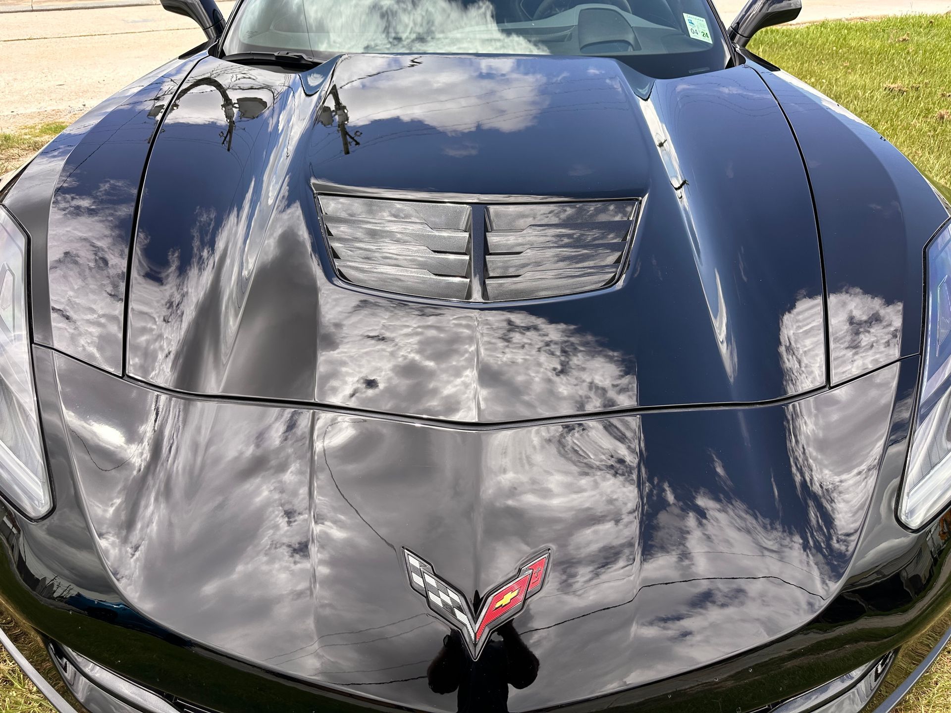 Black Corvette sports car with hood scoop and emblem reflecting sky.