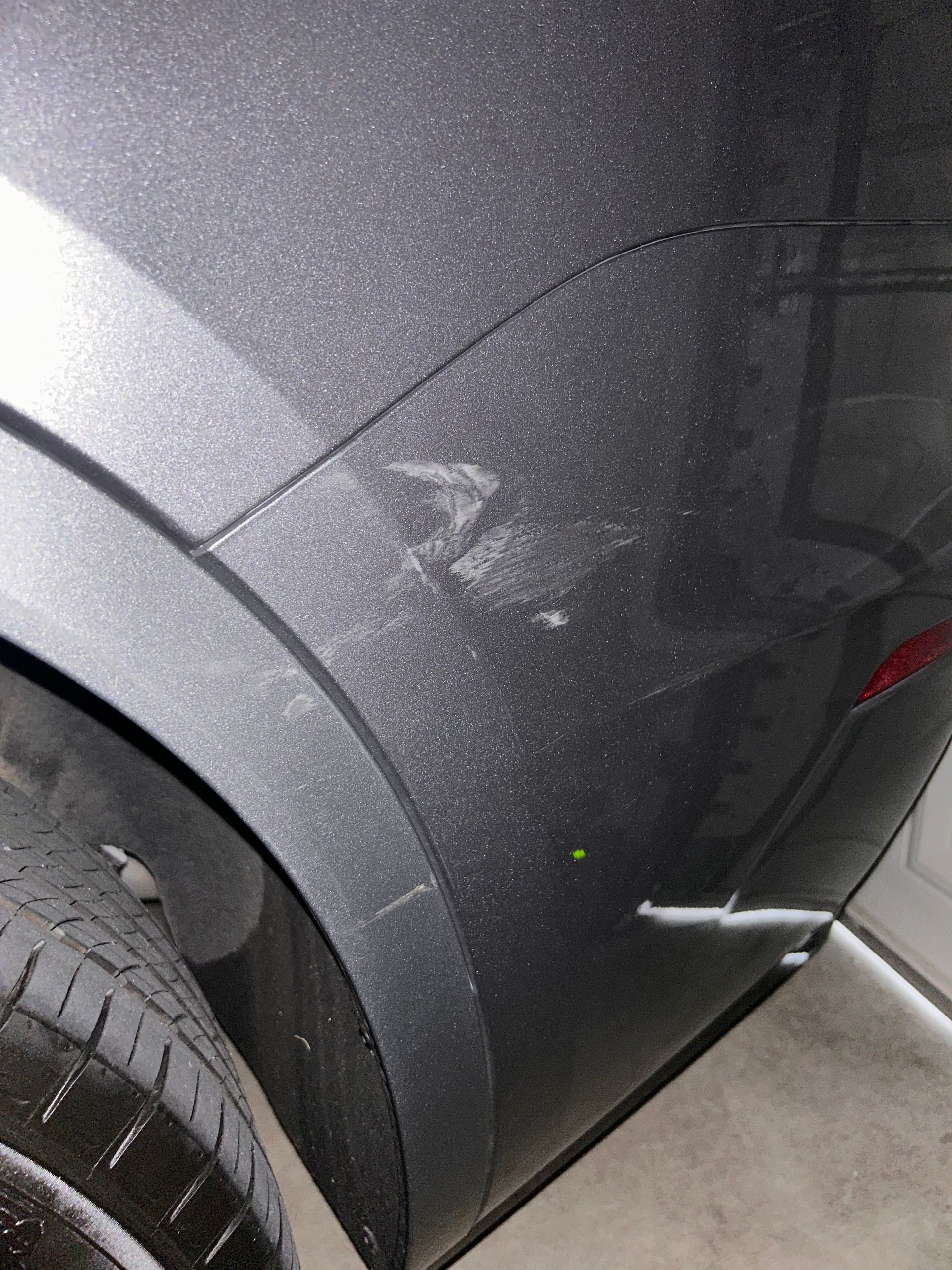 Damaged gray car bumper with scratches and a small dent near the tire.