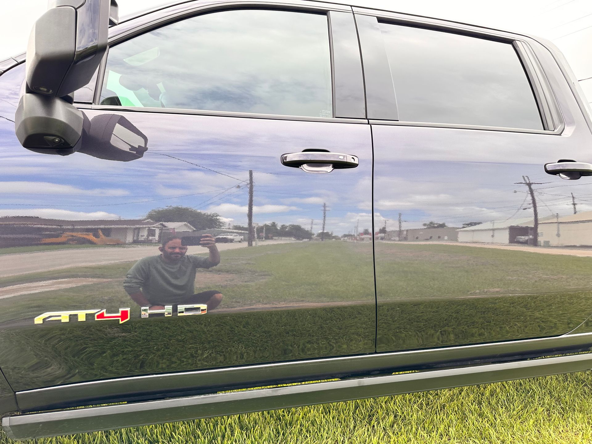 A black pickup truck parked on grass, with a person reflected in the door. The truck has a