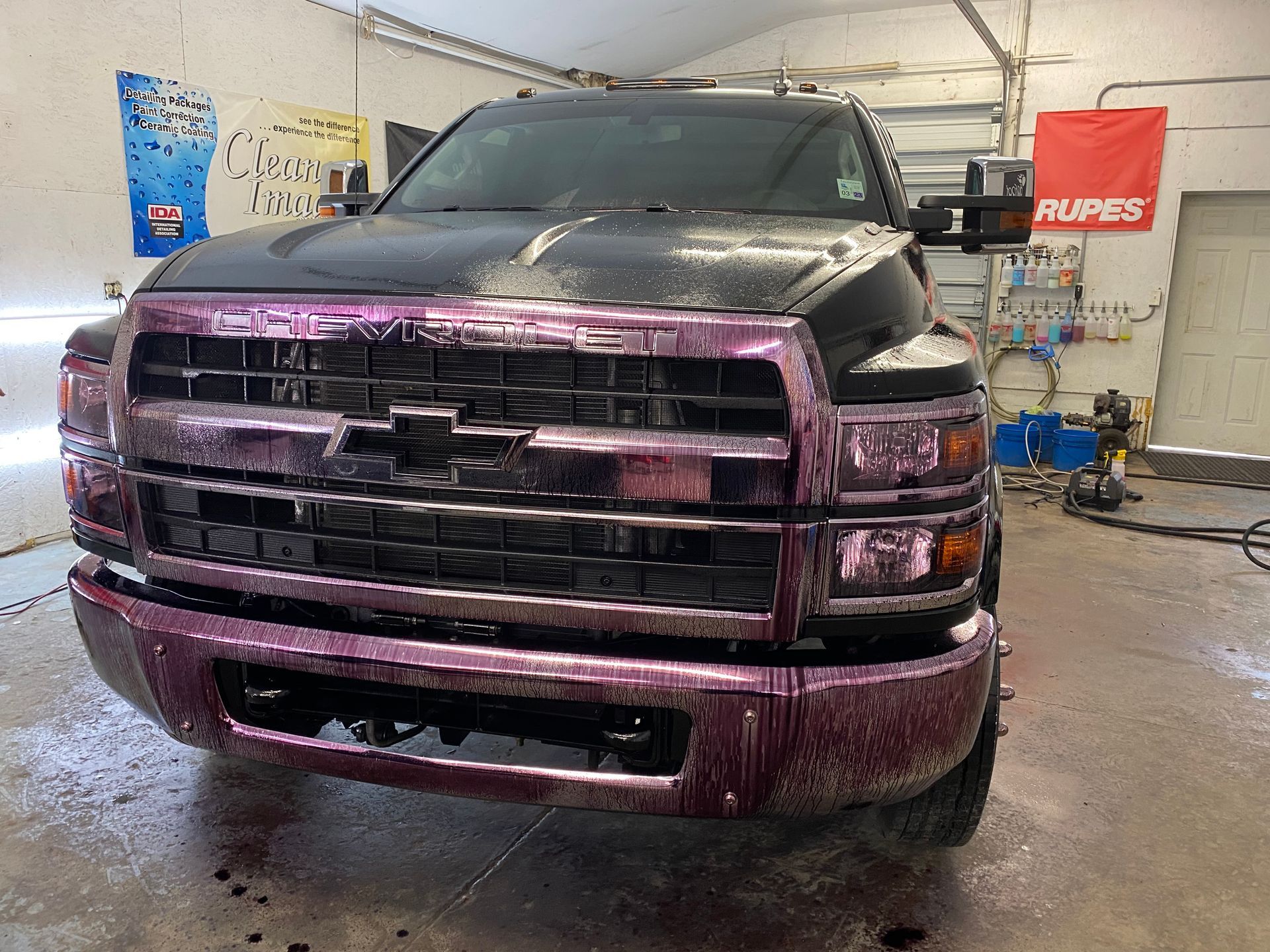 Black pickup truck covered in pink cleaning foam in a garage.