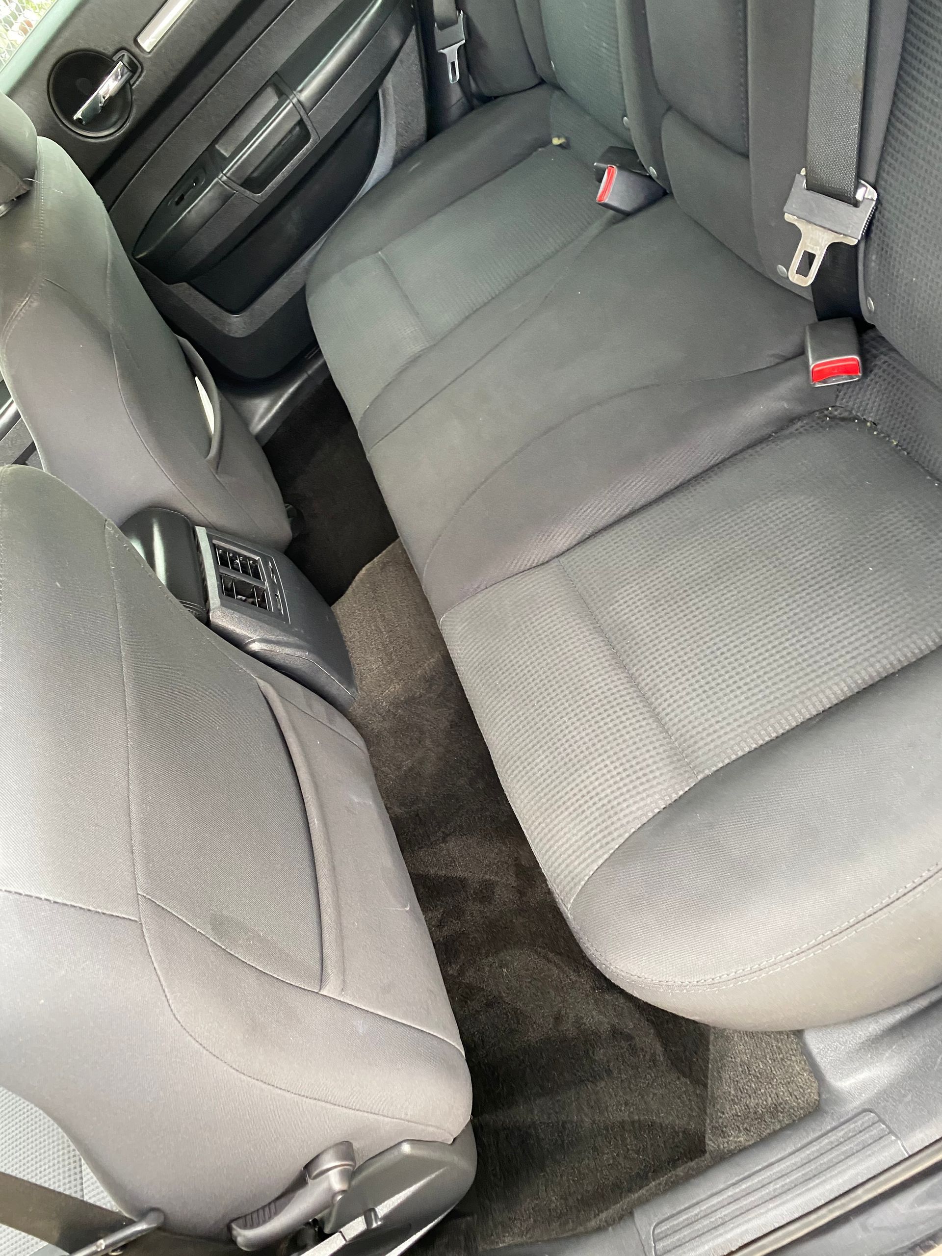 Black car's rear seats and center console with seatbelts. Interior view, fabric seats.