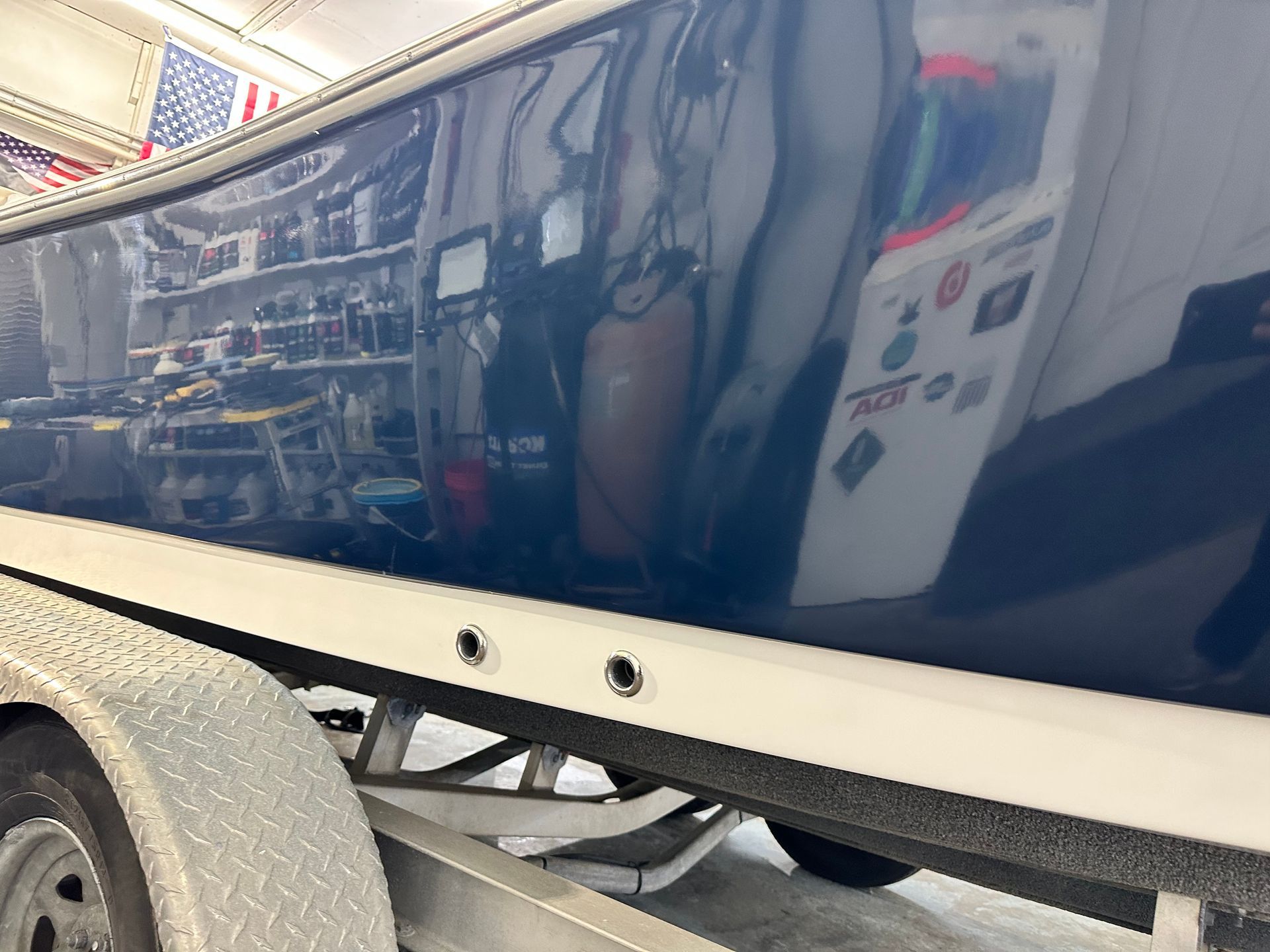 Blue and white boat on a trailer, reflecting a cluttered workshop interior with various items.