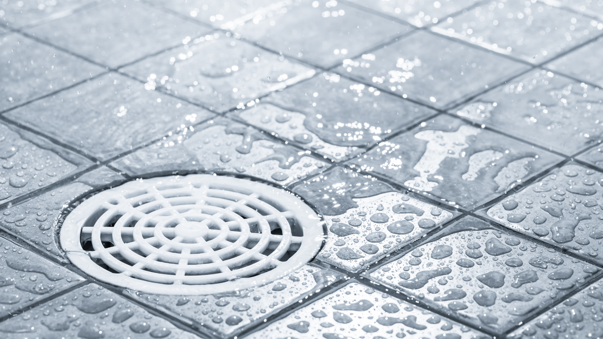 A drain on a tiled floor with water drops on it.