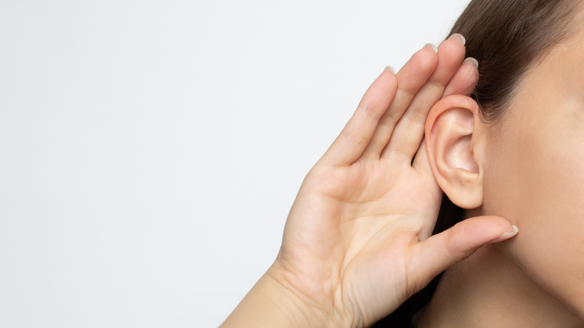 A woman is listening to something with her hand to her ear.
