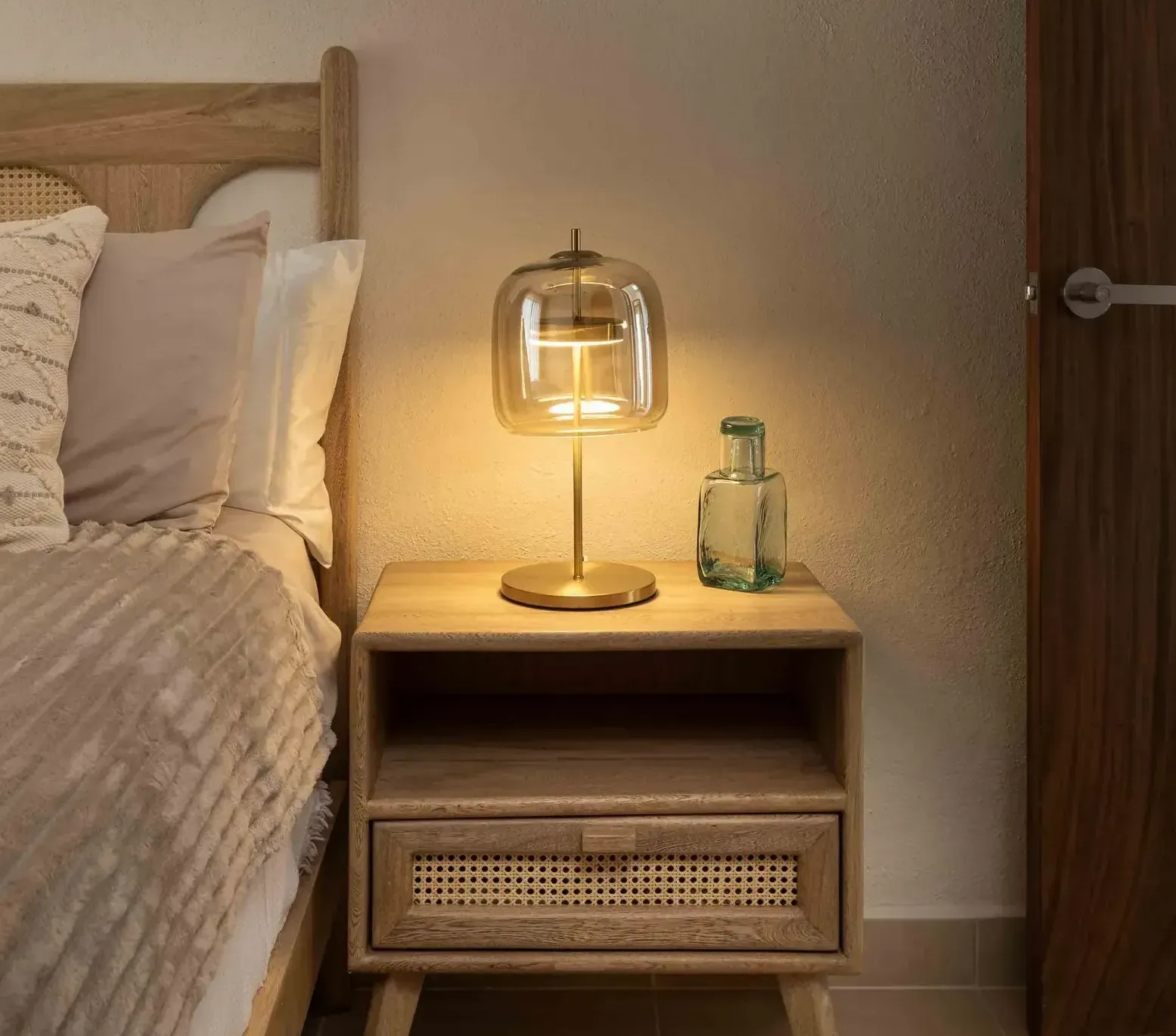 A lamp is sitting on a wooden nightstand next to a bed.