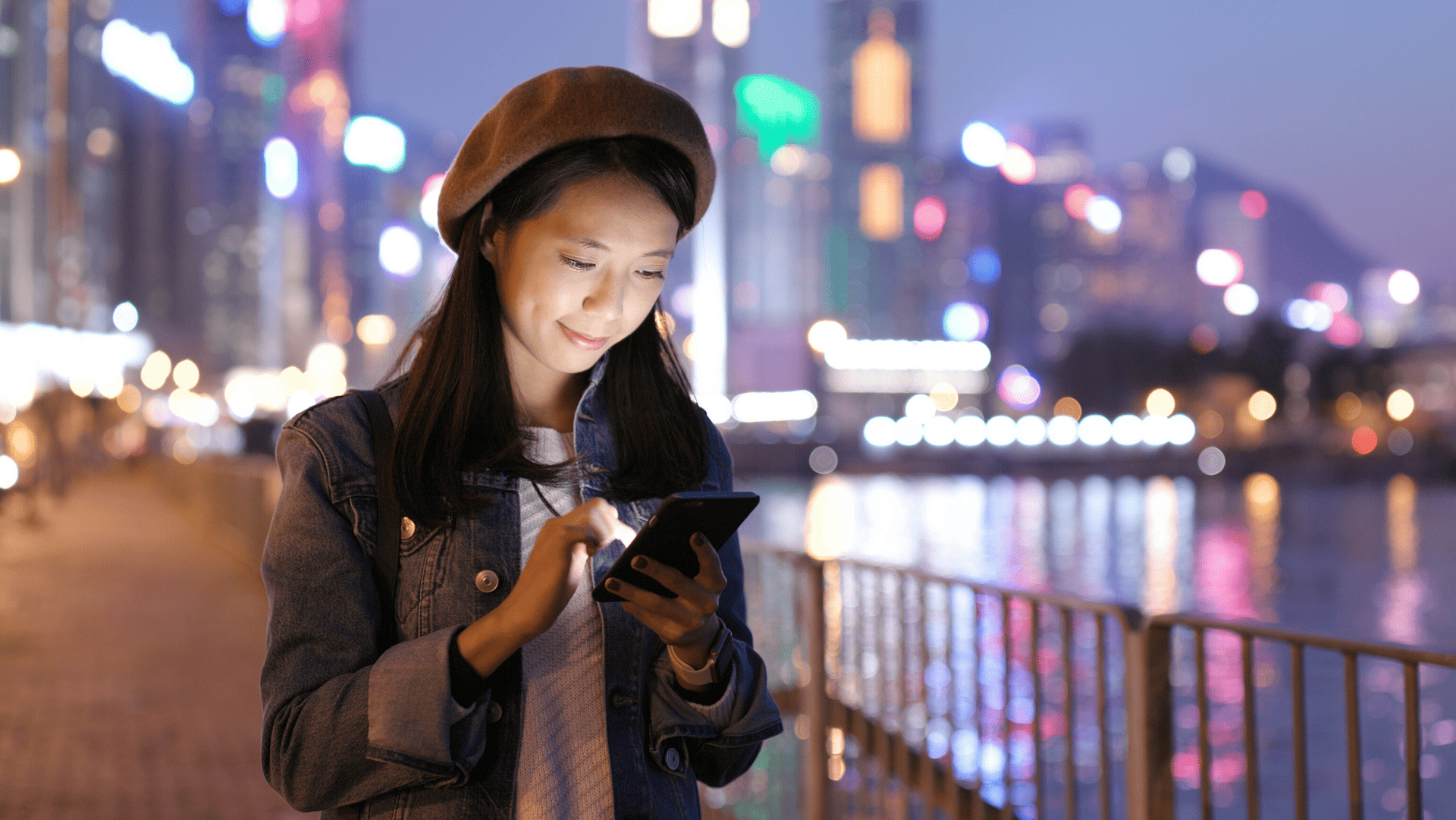 A woman is standing on a bridge looking at her cell phone.