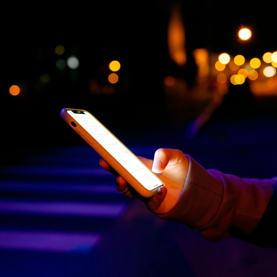 A person is holding a cell phone in their hand at night