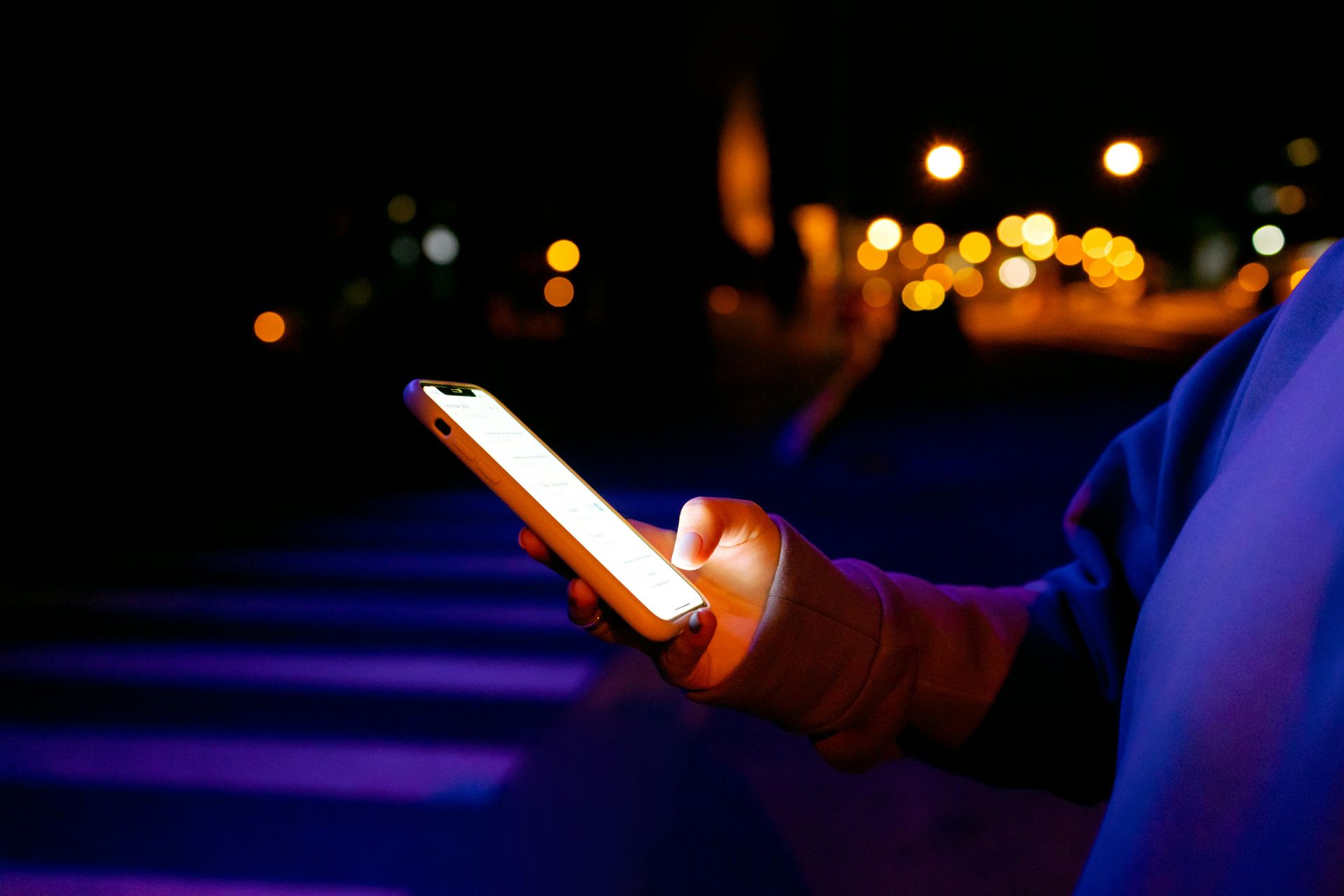 A person is holding a cell phone in their hand at night.