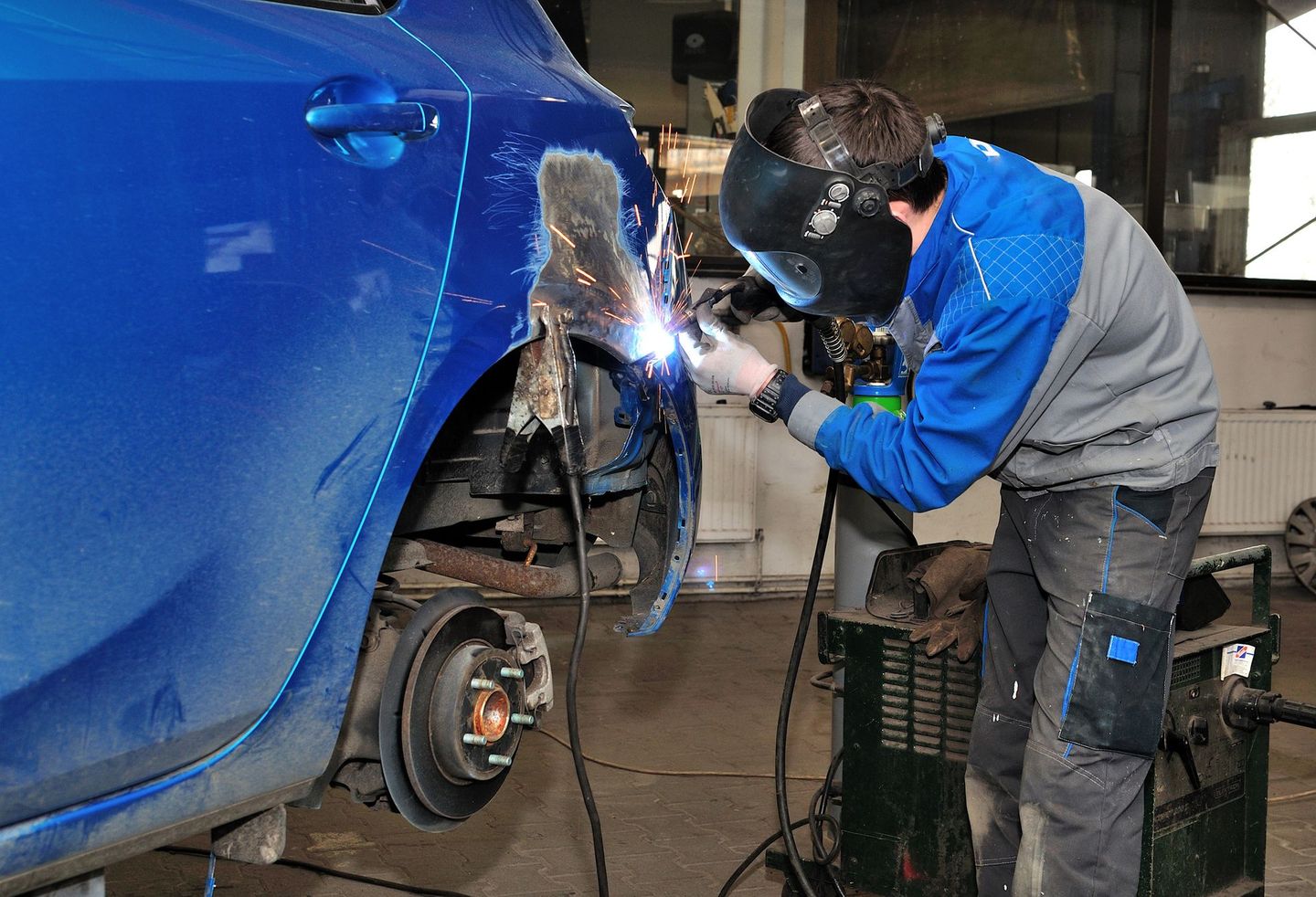A man is welding a blue car in a garage.