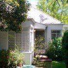 A small white house with a porch surrounded by trees and bushes.