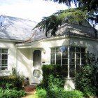 A white house with a gray roof is surrounded by trees and bushes.