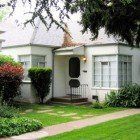 A small white house with a lush green lawn in front of it.