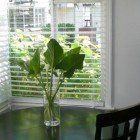 A vase of plants is sitting on a table in front of a window.