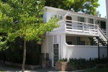A white house with a balcony and stairs is surrounded by trees.