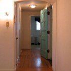 A hallway with hardwood floors and a green door leading to a bathroom.