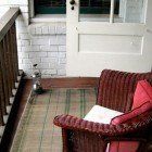 A wicker chair is sitting on a porch next to a door.