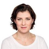 Eine Frau mit einem weißen Hemd und einer Halskette blickt in die Kamera.