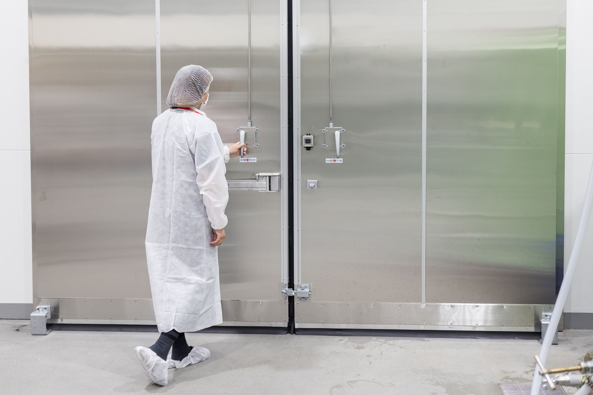 A woman in a white gown is standing in front of a stainless steel door.