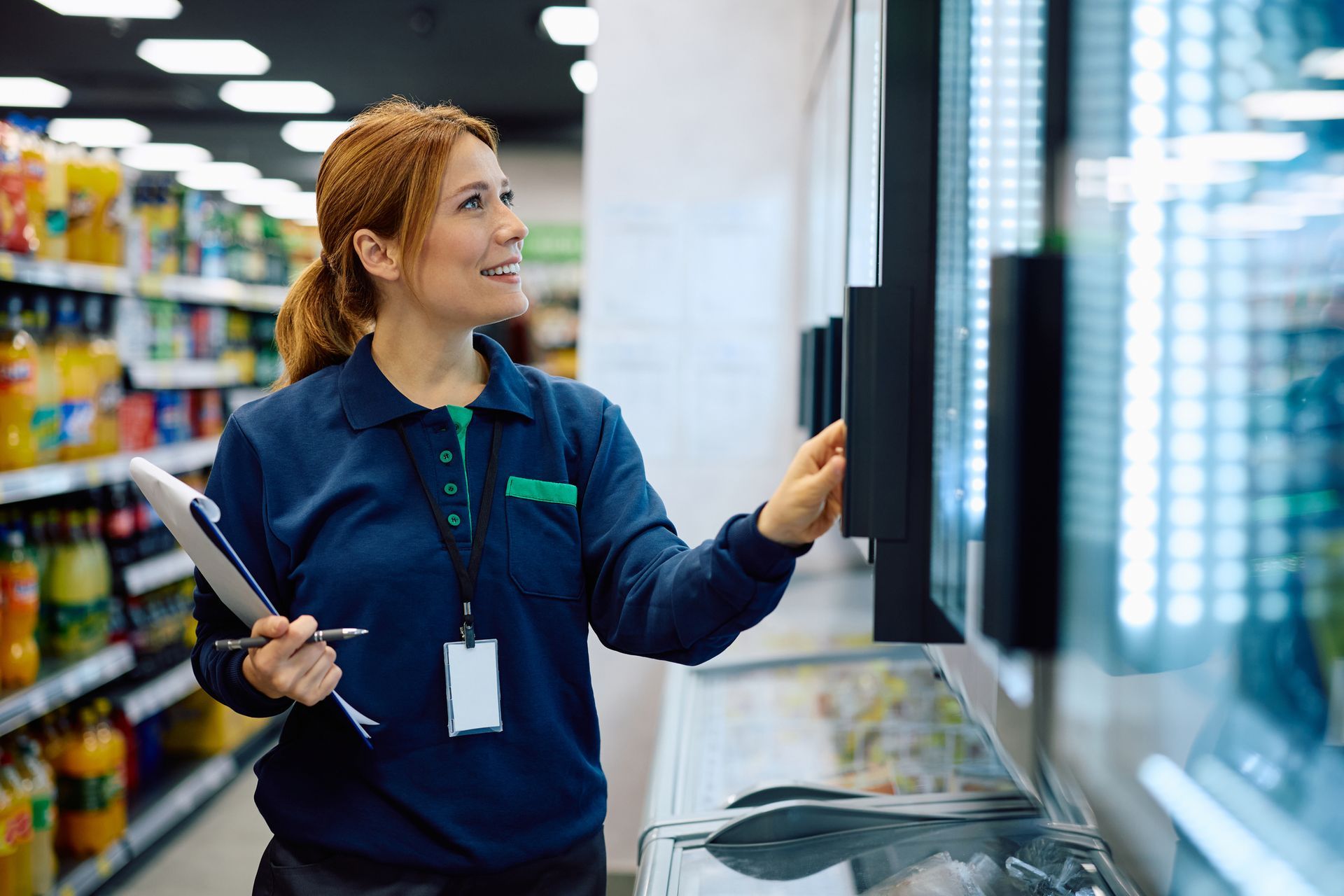 Happy female supermarket manager checking stock of products in refrigerated section.