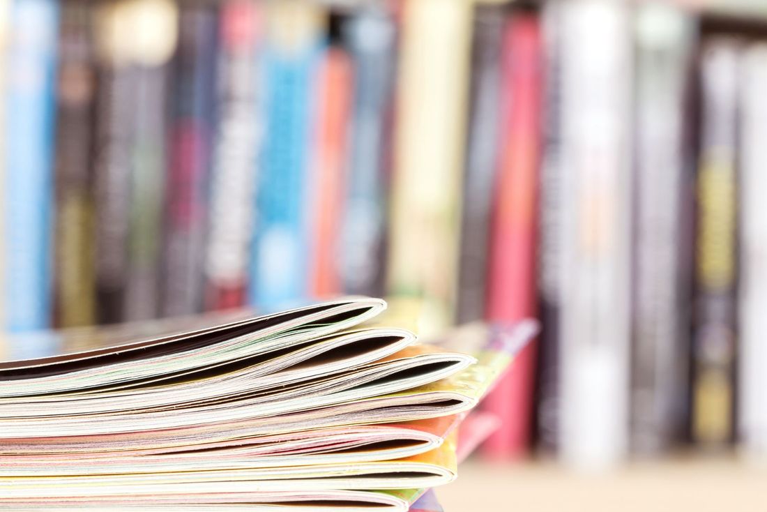 Una pila di riviste è appoggiata su un tavolo di fronte a una libreria.