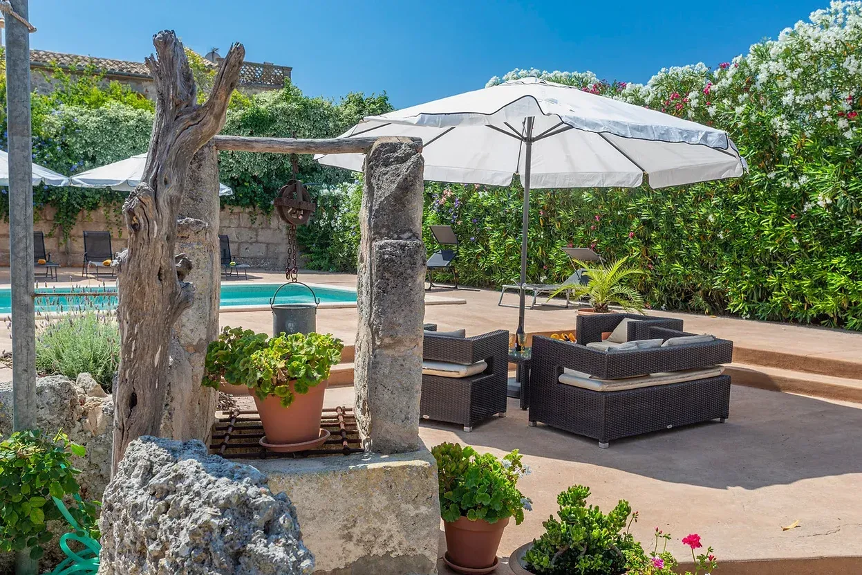 Un patio con piscina, sillas, sombrillas y plantas en macetas.