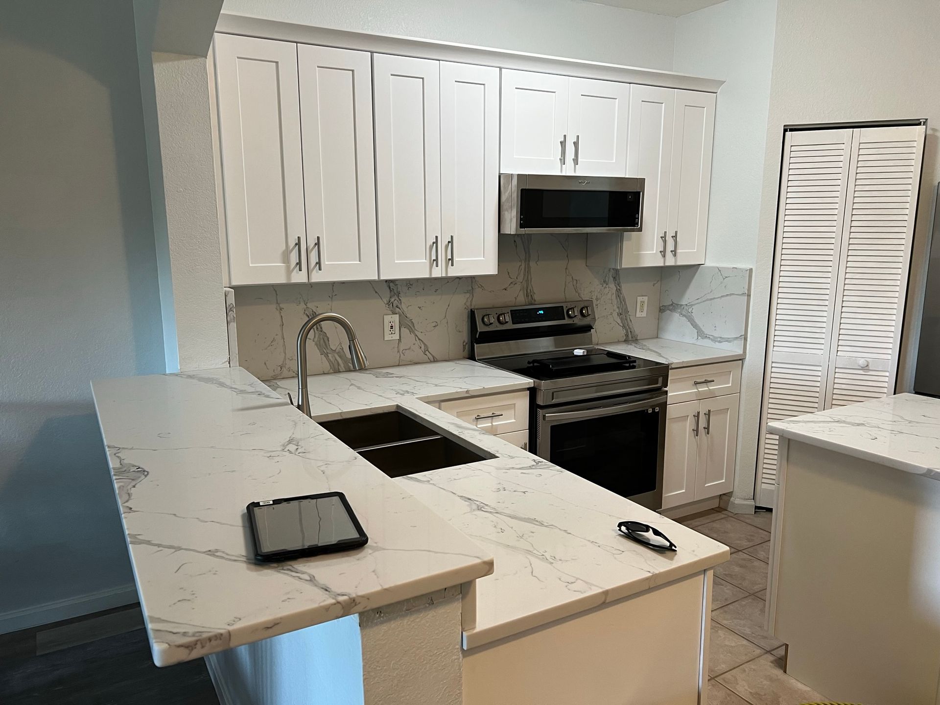 Modern white kitchen with marble-look countertops, stainless stove, sink, and wall cabinets