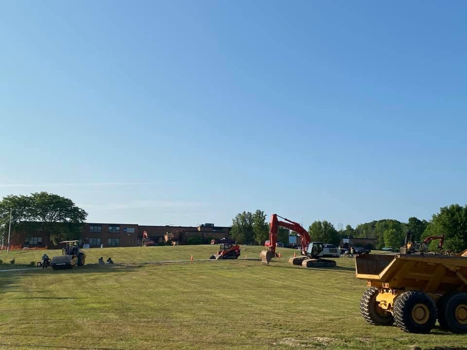 Construction equipment on a grassy field under a clear blue sky, with excavators and a dump truck.