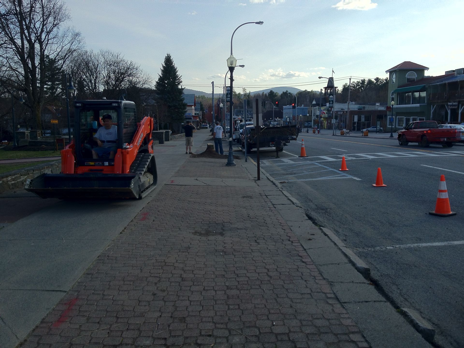 Roadwork scene with an orange construction vehicle, traffic cones, and lane closures along a street.