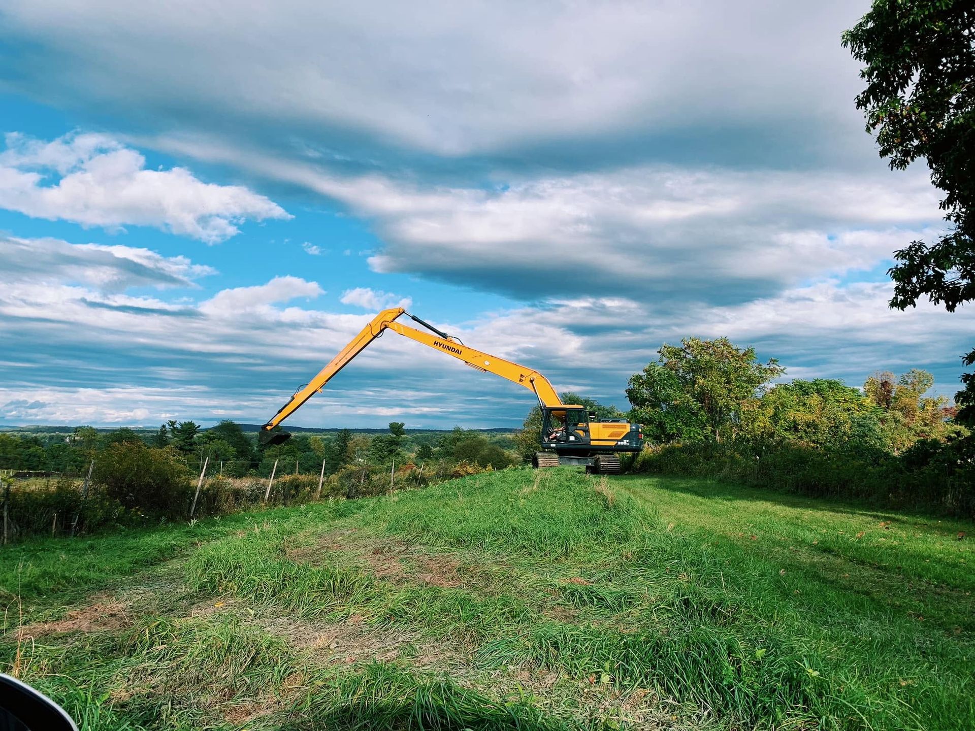 Yellow excavator working on a grassy field under a cloudy blue sky