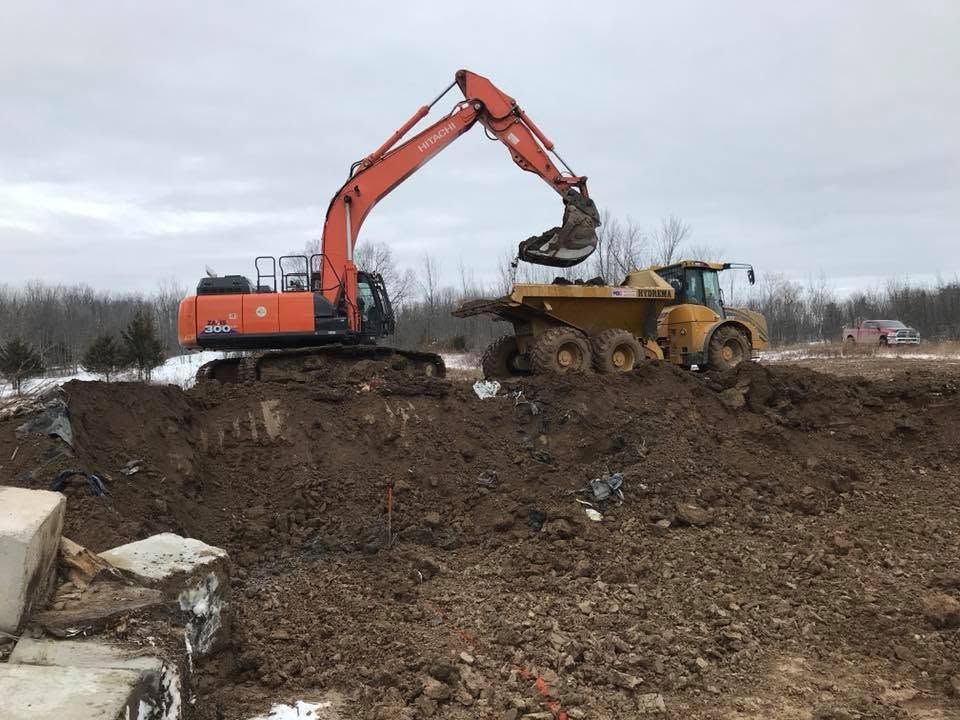 Excavator loading dirt into a yellow dump truck at a muddy construction site