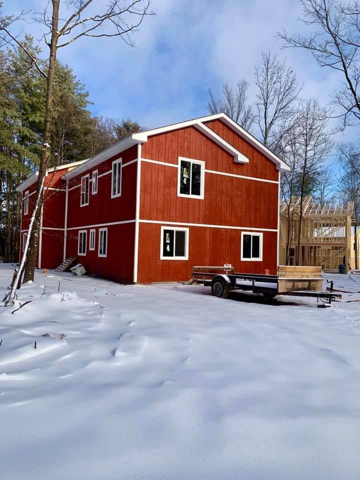 Red two-story house in a snowy yard with bare trees and a blue sky