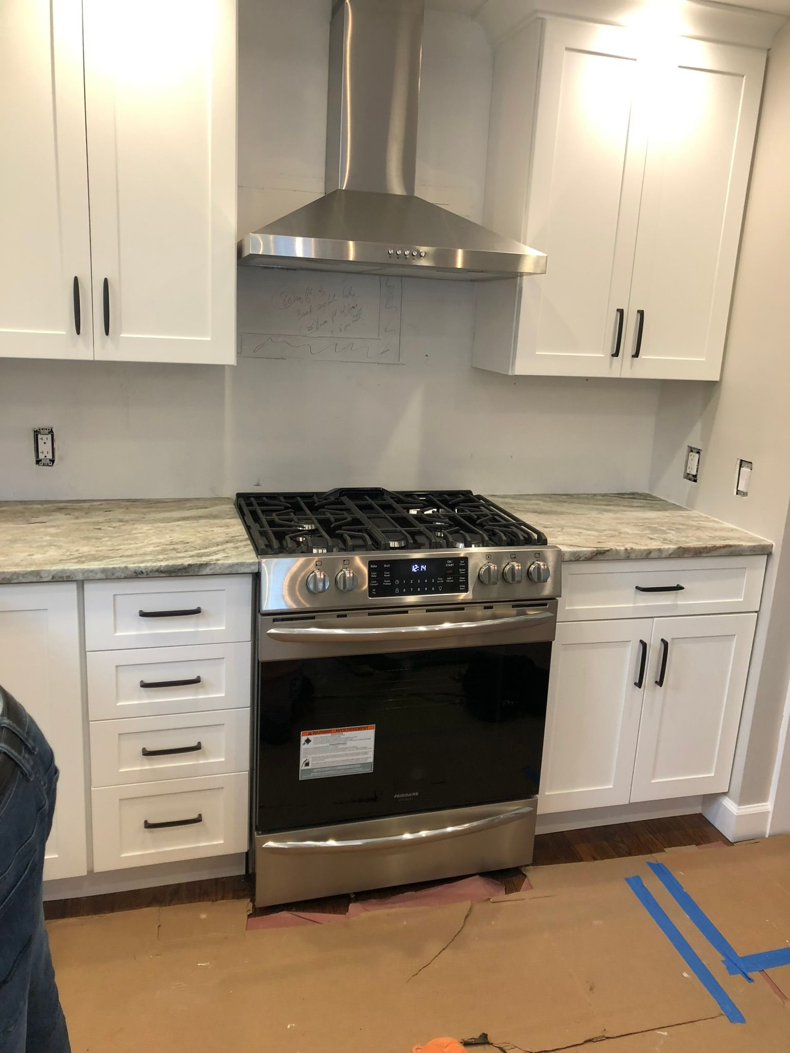 New kitchen with white cabinets, granite counters, stainless steel stove and range hood, and cardboard on the floor