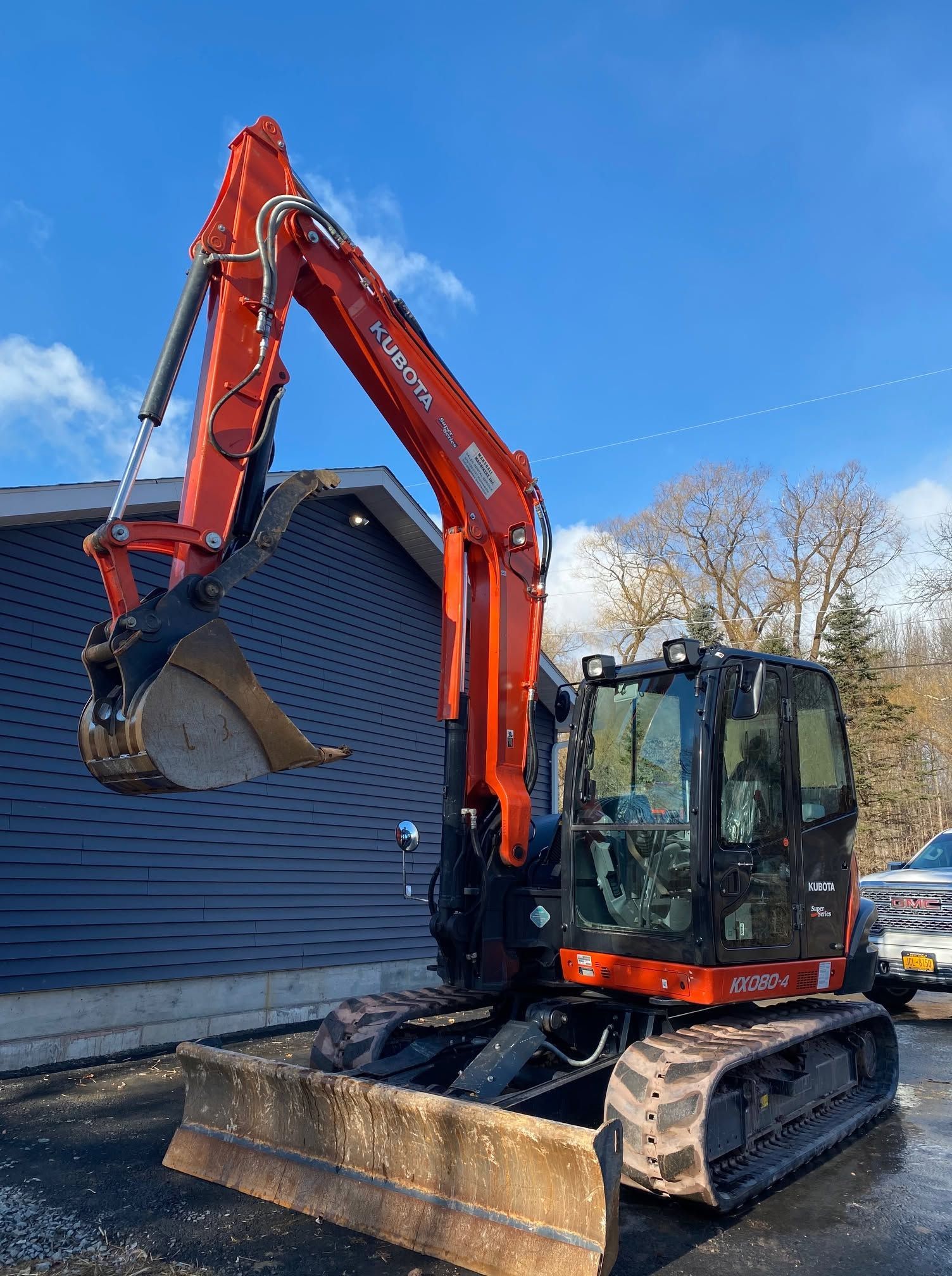 Orange excavator lifting debris beside a house on a snowy site