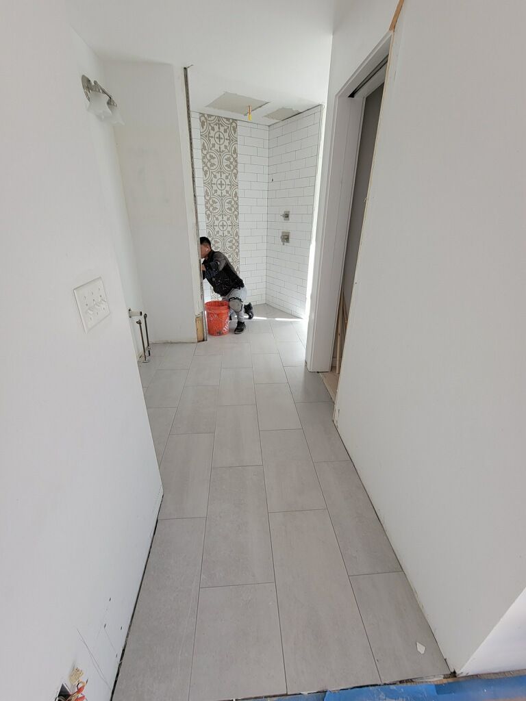 Narrow white hallway with tiled floor; person crouches near cleaning supplies at the far end.