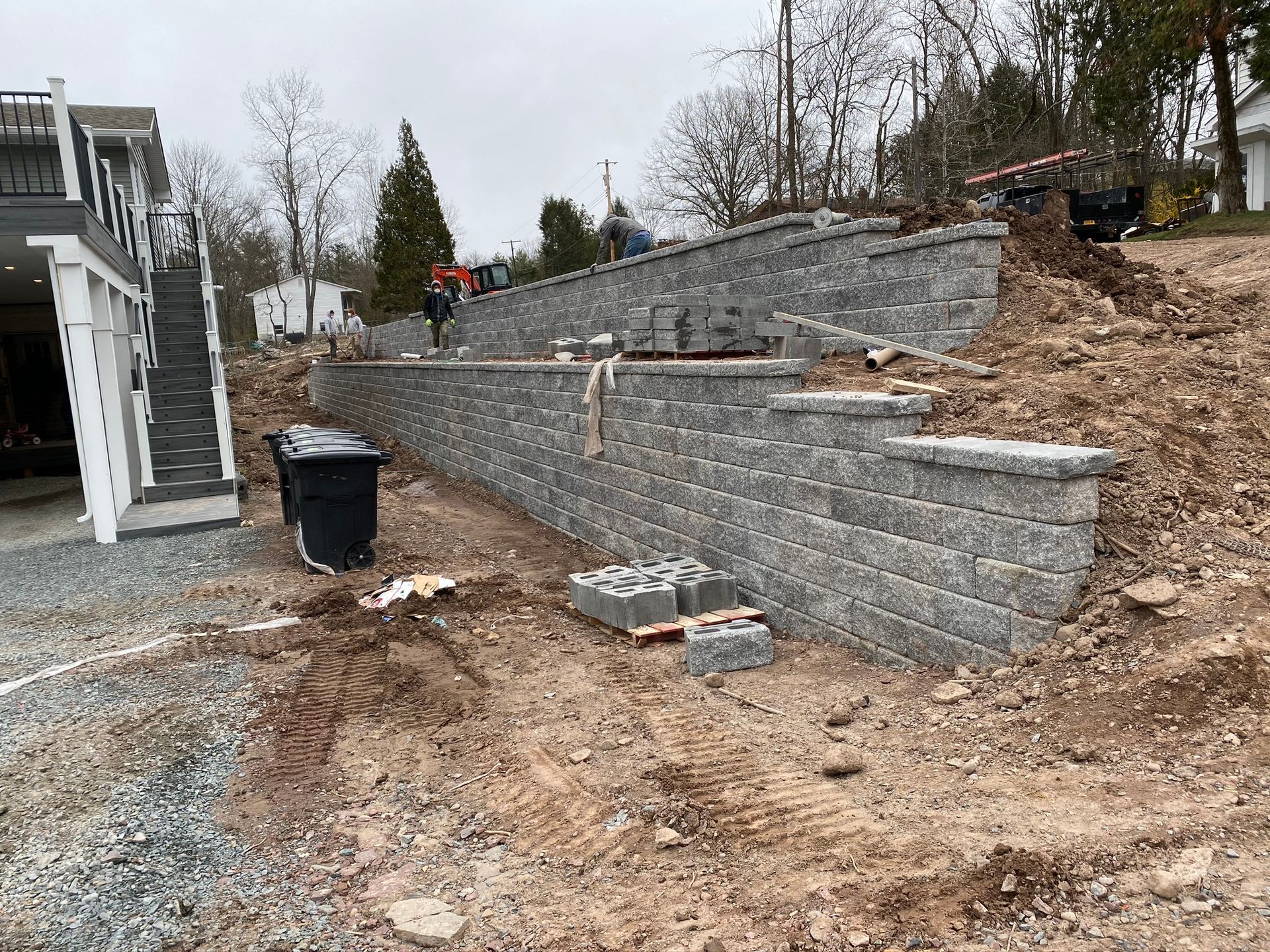 Terraced gray stone retaining walls along a muddy hillside beside a house and driveway.
