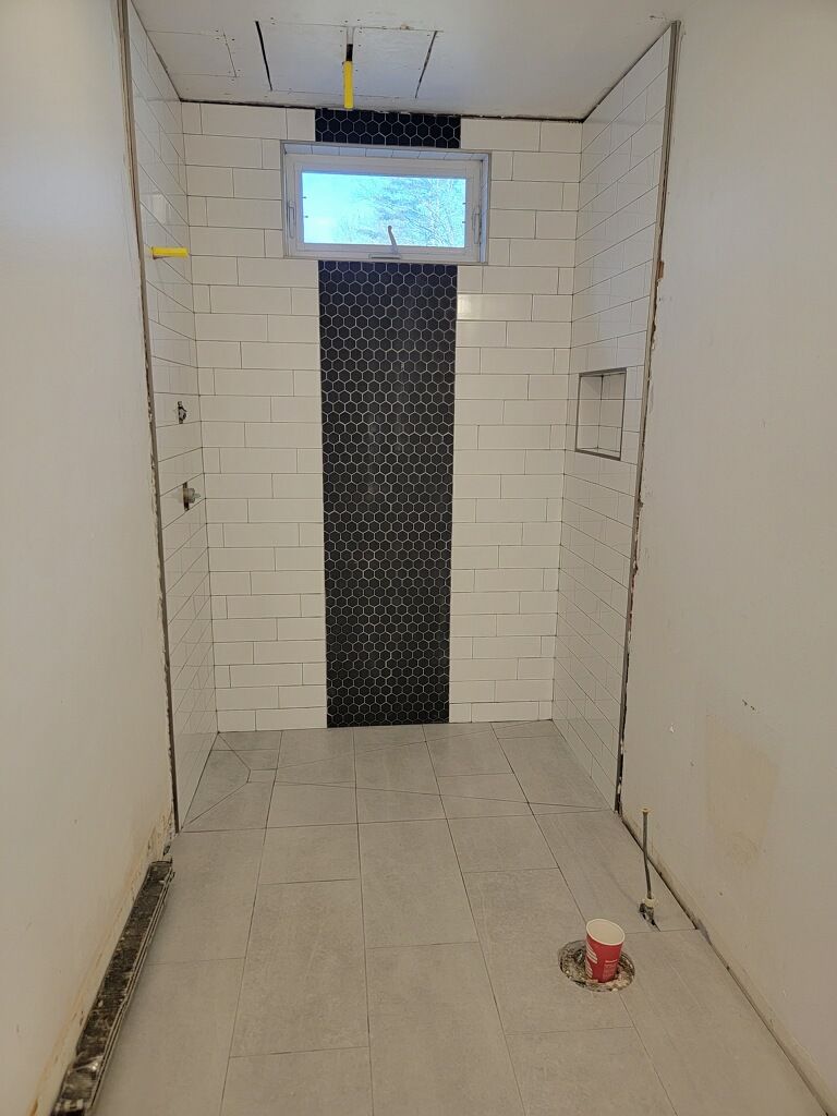 Narrow tiled room with a centered doorway, small window, and a red object on the floor.