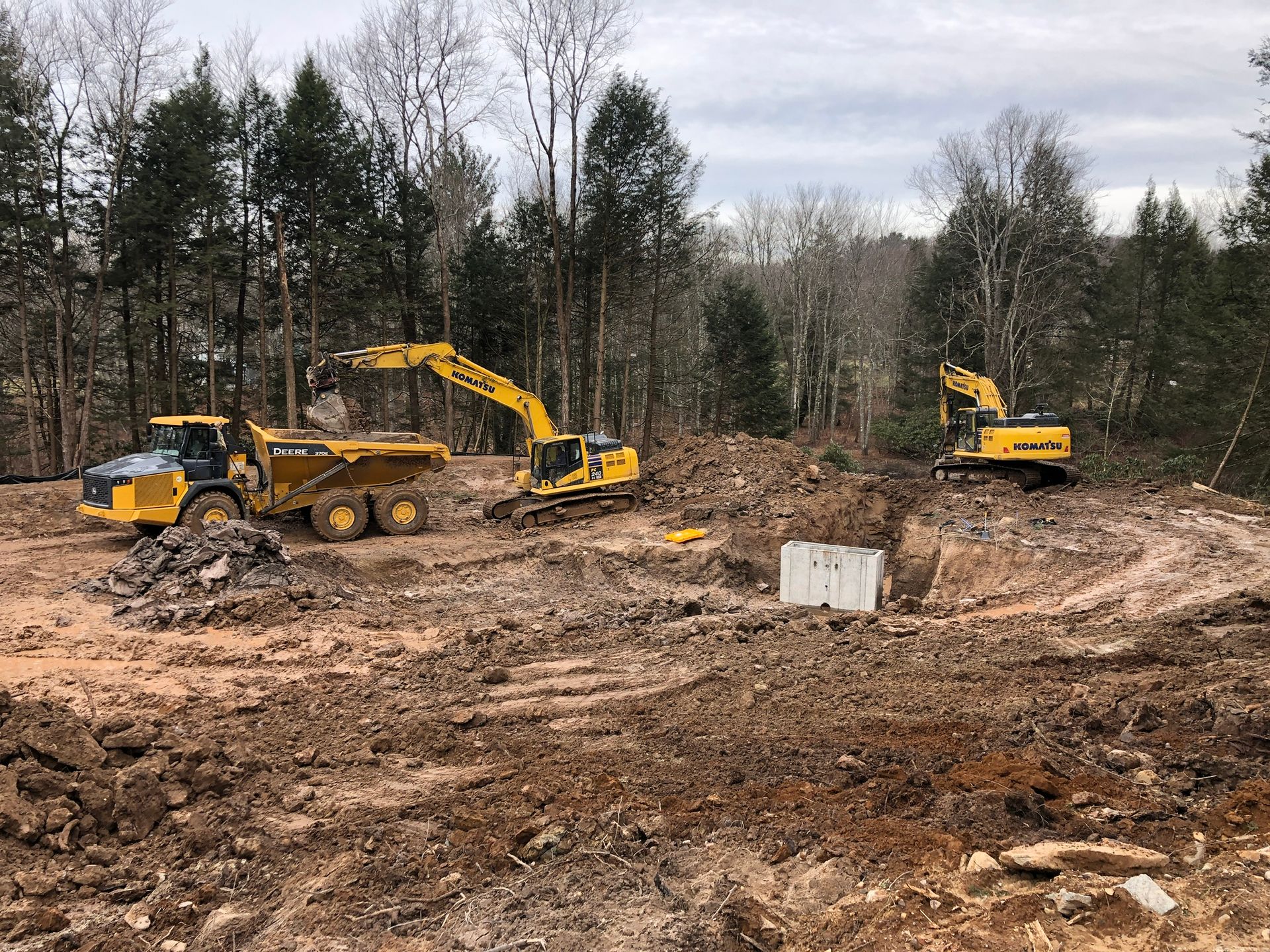 Yellow excavators and a dump truck on a muddy construction site beside a wooded area