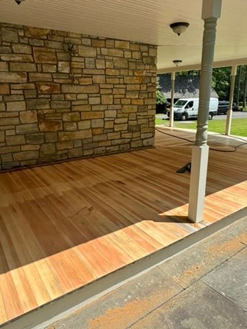 Covered porch with stone wall, wood floor, white columns, and a parked car in the background.